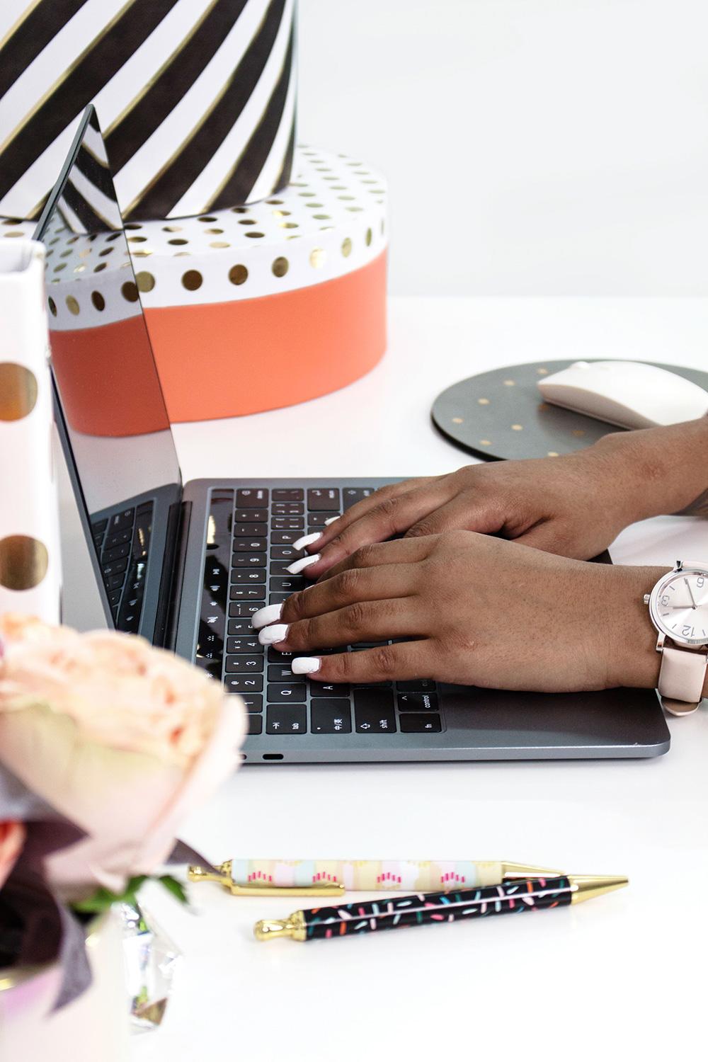 african american woman typing on her macbook at a desk with roses and organizing boxes nearby